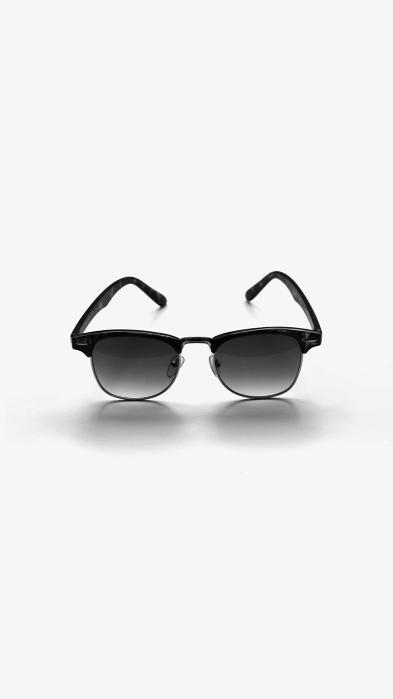 Black browline sunglasses seen from the front, standing on a white table with a soft shadow under them.