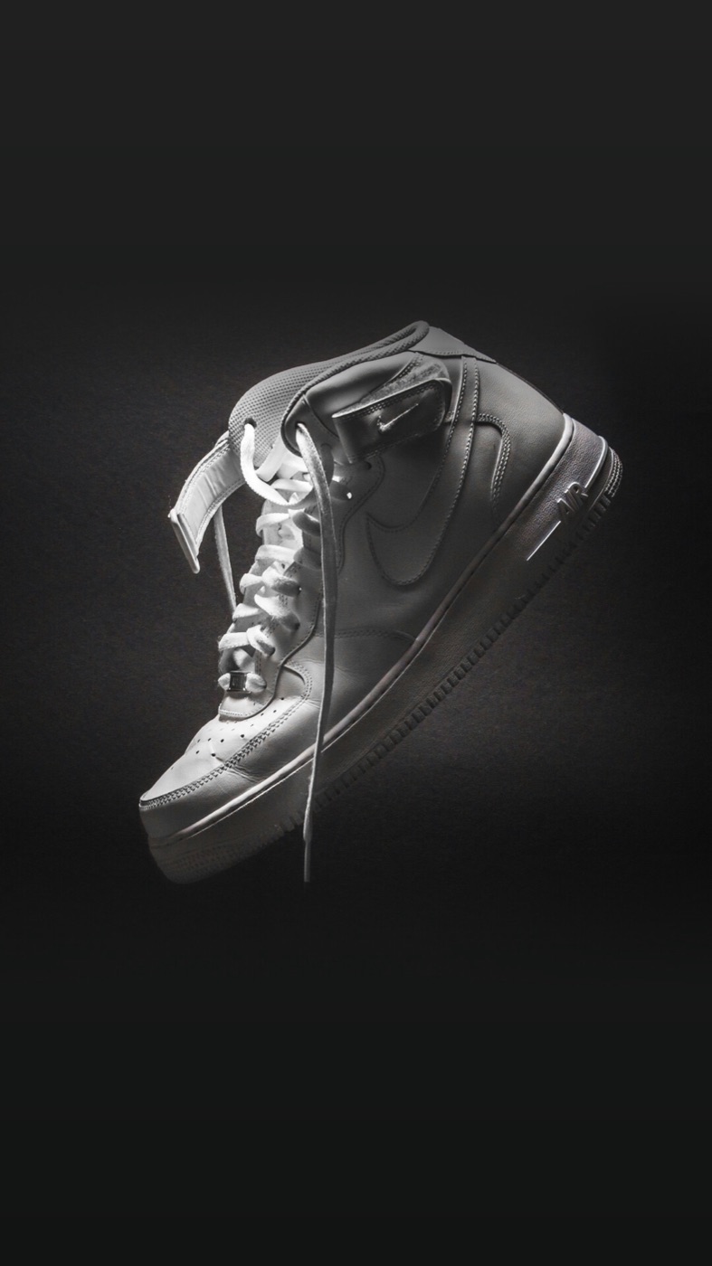 A white leather high-top with its laces loose, lit from above against a black background.
