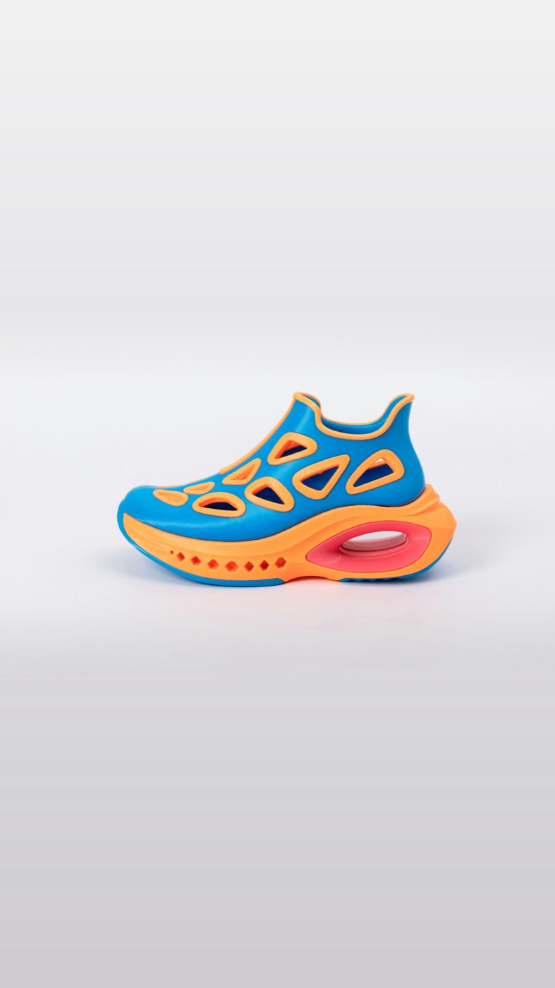 The Hyper Flow Runner on a plain light grey backdrop: a blue knit upper with orange cut-out panels, on an orange sole with a pink air window.